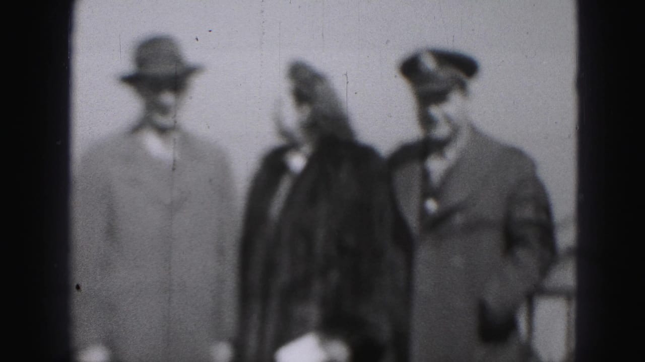 Three adults walking, with the woman turned toward the man in a peaked cap.