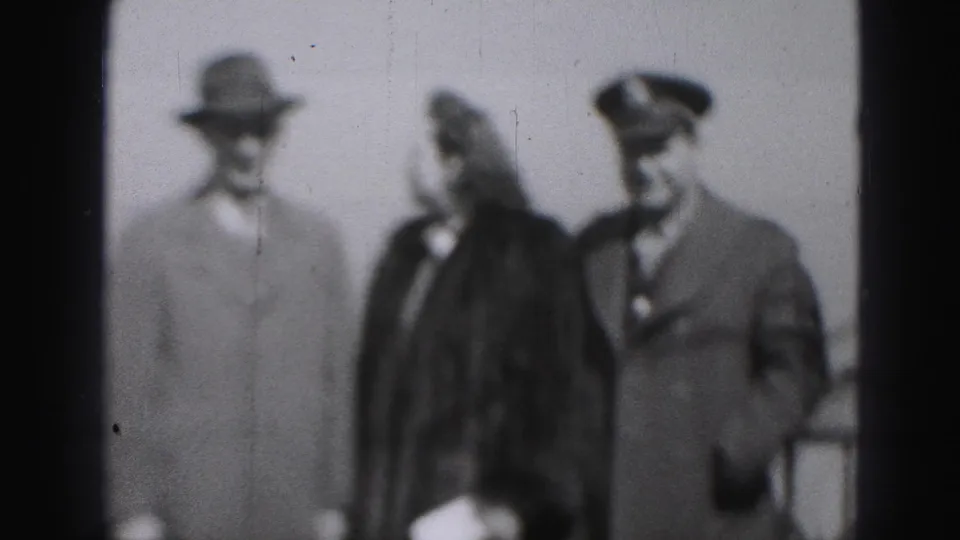 Black-and-white home-movie frame from Harrisburg showing the woman turned toward a man in a military-style cap as they walk.