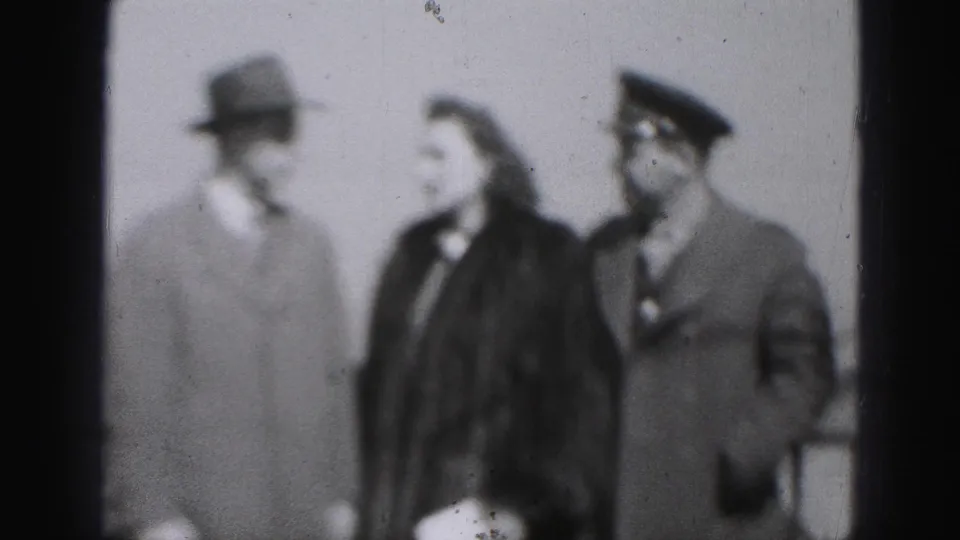 Closer soft-focus 1946 Harrisburg frame of three adults in formal outerwear, including a fedora and a military-style peaked cap.