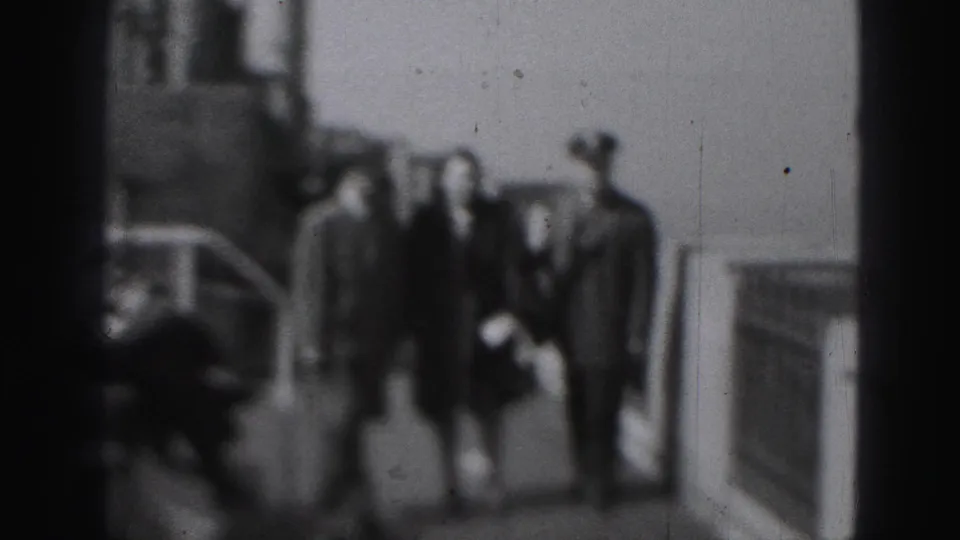 Wider black-and-white Harrisburg frame showing the walking group near railings, with a faint vehicle shape in the background.