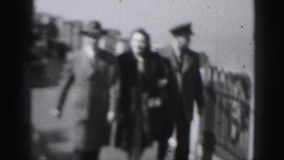 A soft-focus 1946 Harrisburg frame shows the woman, hatted man, and police officer nearing the camera on the walkway.