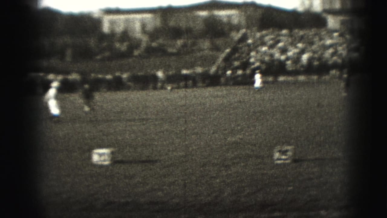 Wide 1946 Harrisburg sports frame with players on a grass field, numbered markers, sideline spectators, and crowded bleachers.