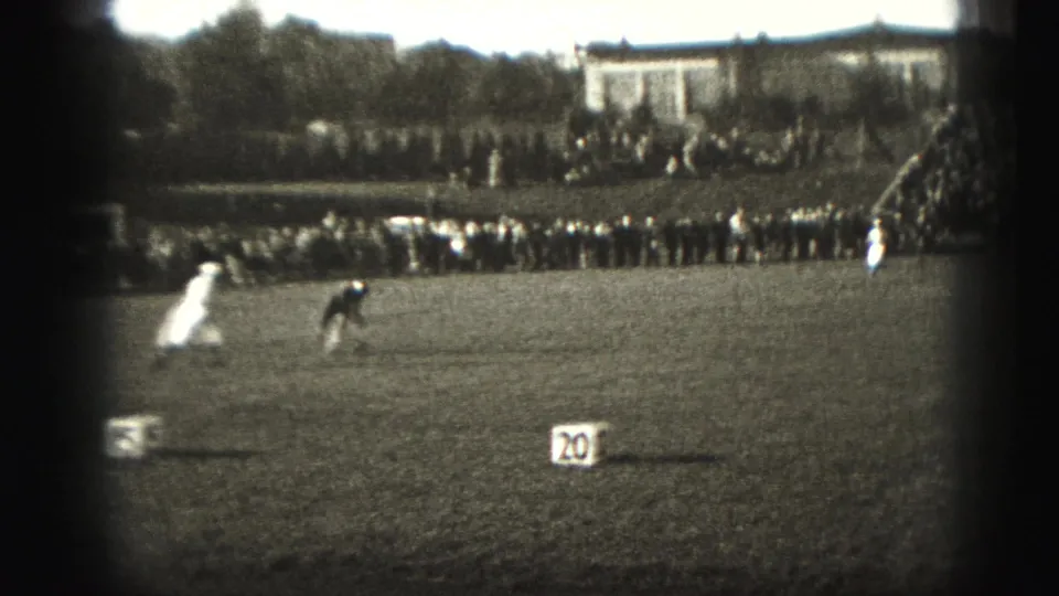 1946 Harrisburg frame showing two athletes in motion on a grass field, with a crowd and bleachers beyond the sideline.