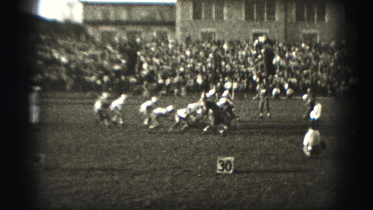 Football players line up near a 30-yard marker with a large crowd in bleachers behind them.