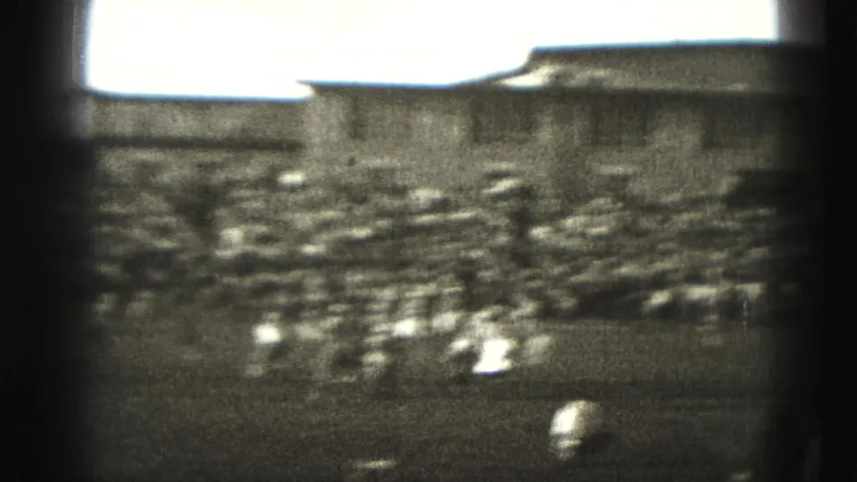 Motion-blurred 1940s football action moves across the field, with bleachers and a large building visible beyond the play.