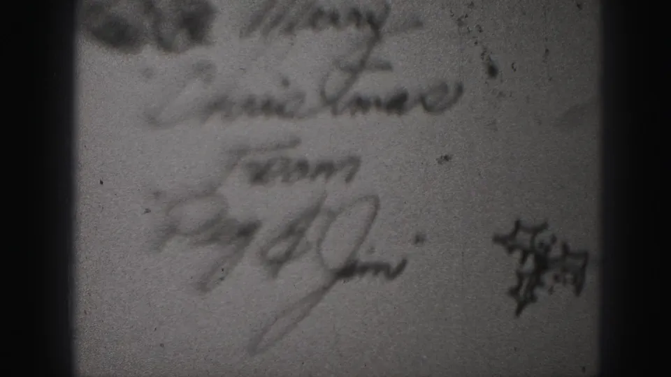 Close 8mm view of cursive writing on a paper item, with a small dark graphic at right and heavy softness from the film capture.