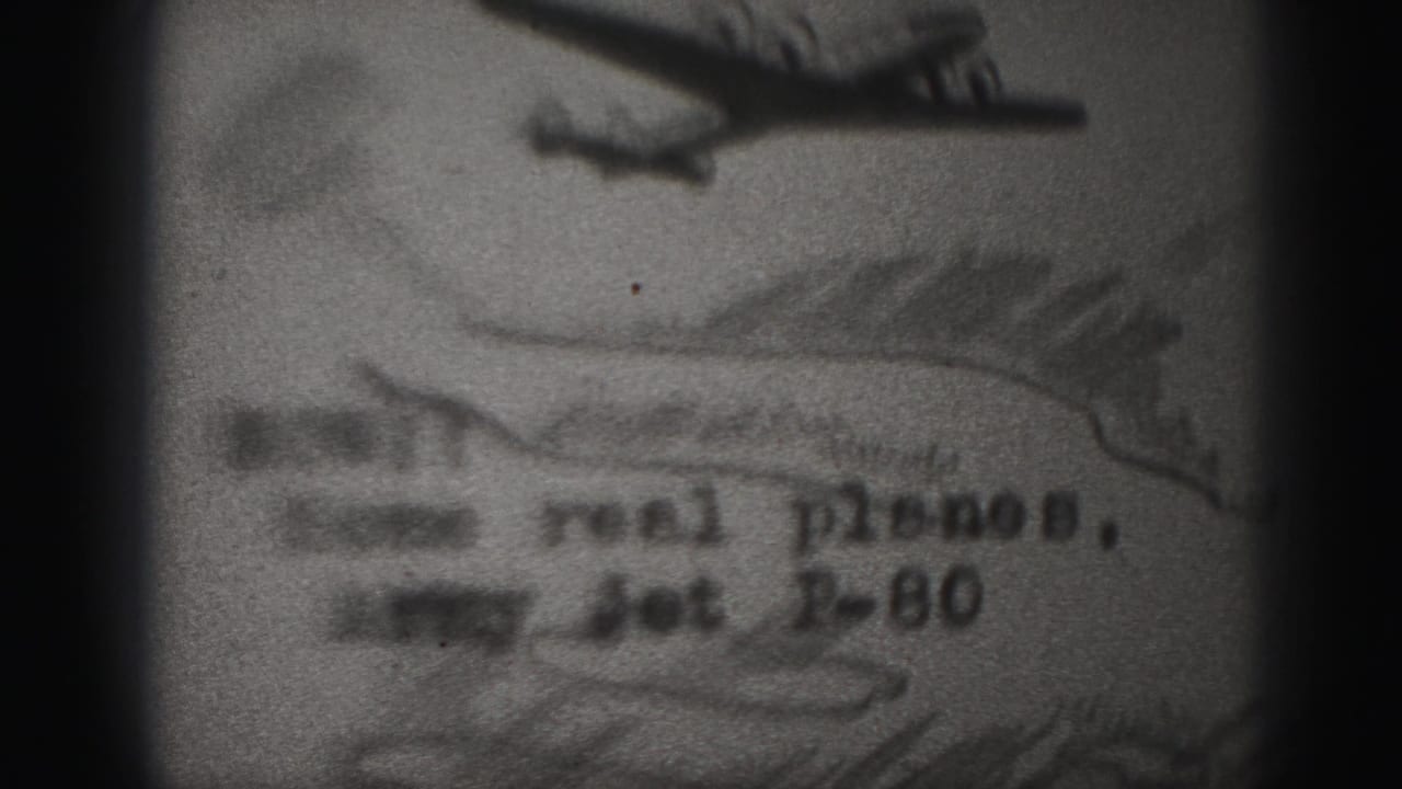 Grainy frame of a plane picture with partial handwritten or filmed title text.