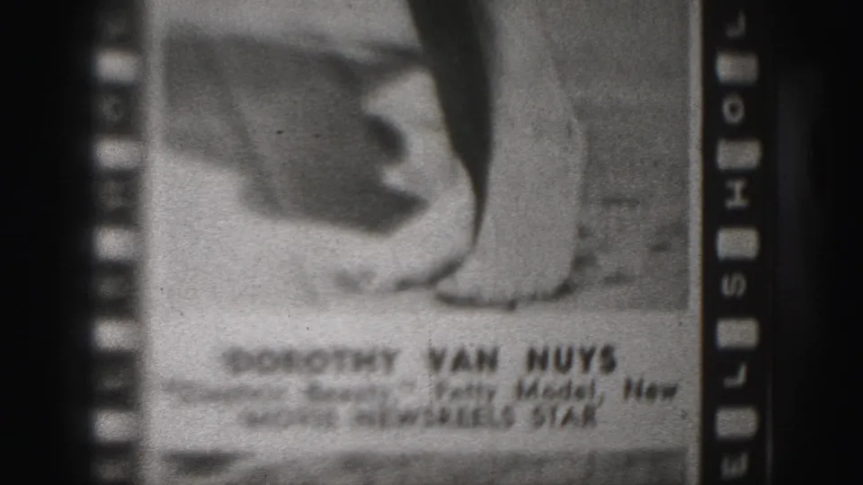 Black-and-white 8mm frame of a filmed Dorothy Van Nuys still, showing legs, lower-edge caption text, and sprocket-side markings.