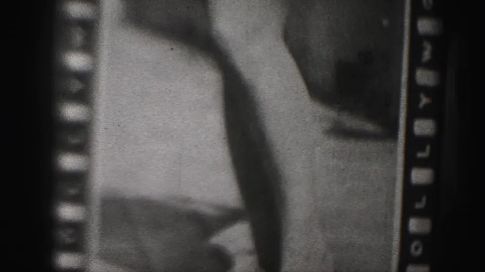Final 8mm frame showing the lower portion of the filmed Dorothy Van Nuys still, with legs, heavy grain, and sprocket-edge markings.