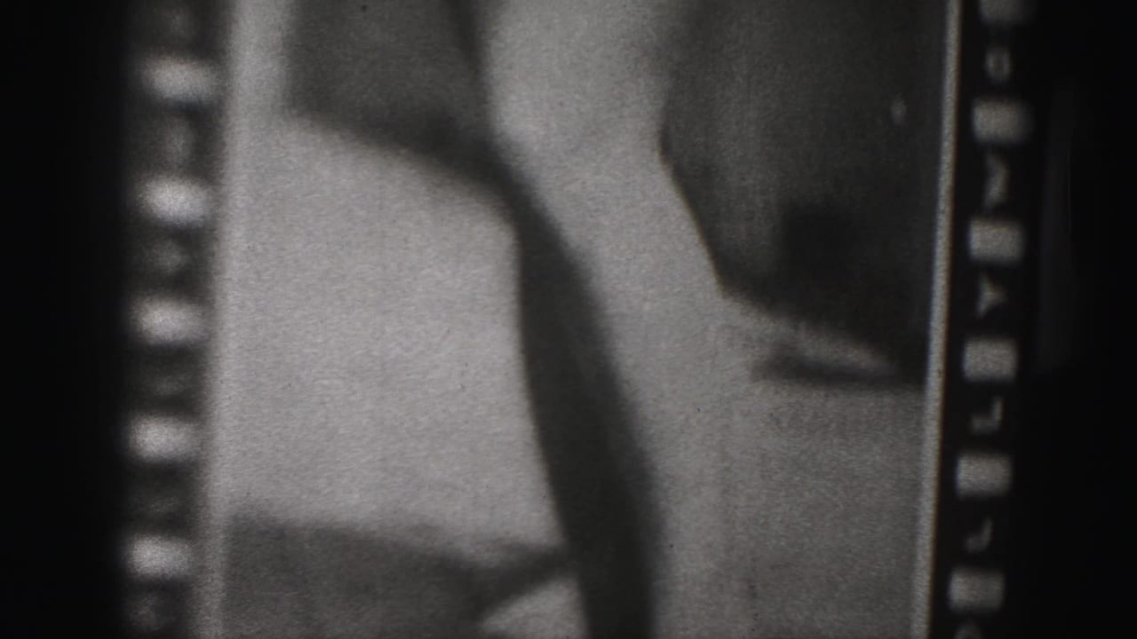 Cropped black-and-white frame of a woman's legs and lower garment beside visible film sprocket edges.