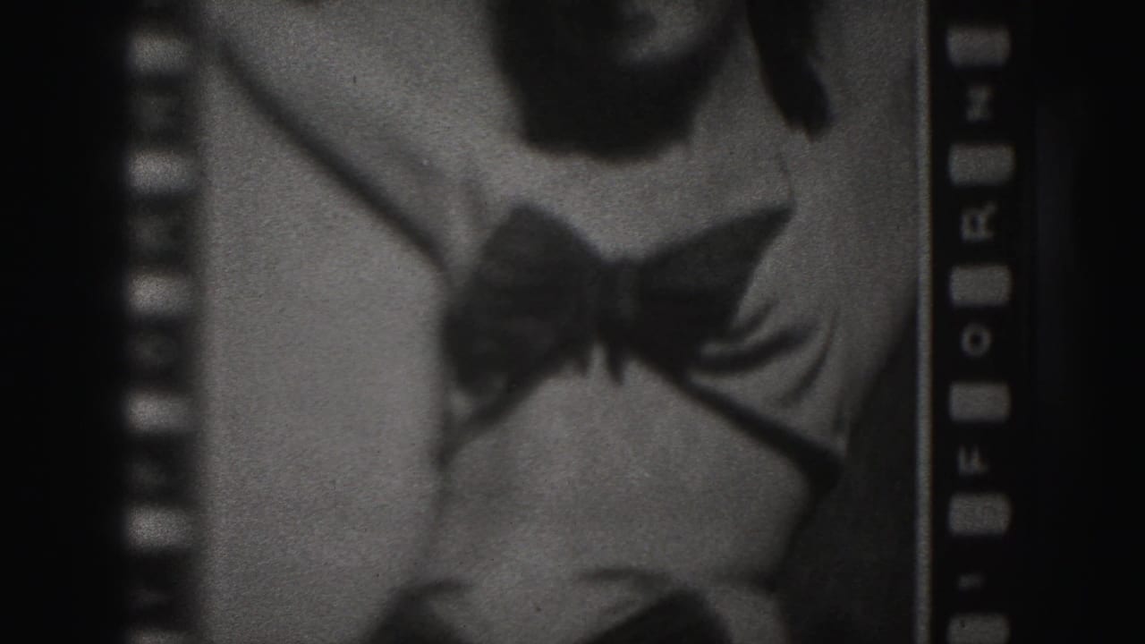 Woman in a dark one-piece bathing suit seen in a grainy film frame with sprocket edges.