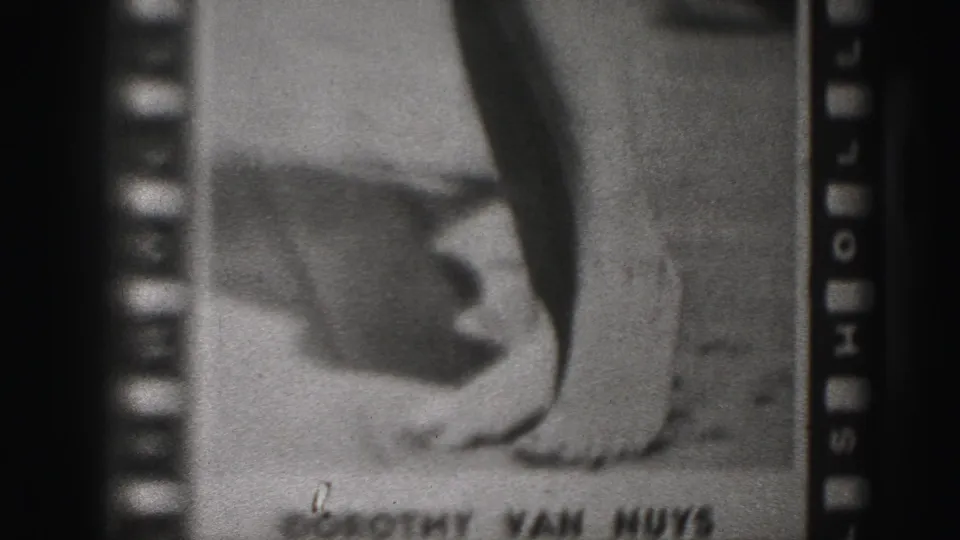 Grainy 8mm frame from the Harrisburg 1946 clip showing the lower poster with shoes and emerging caption text.