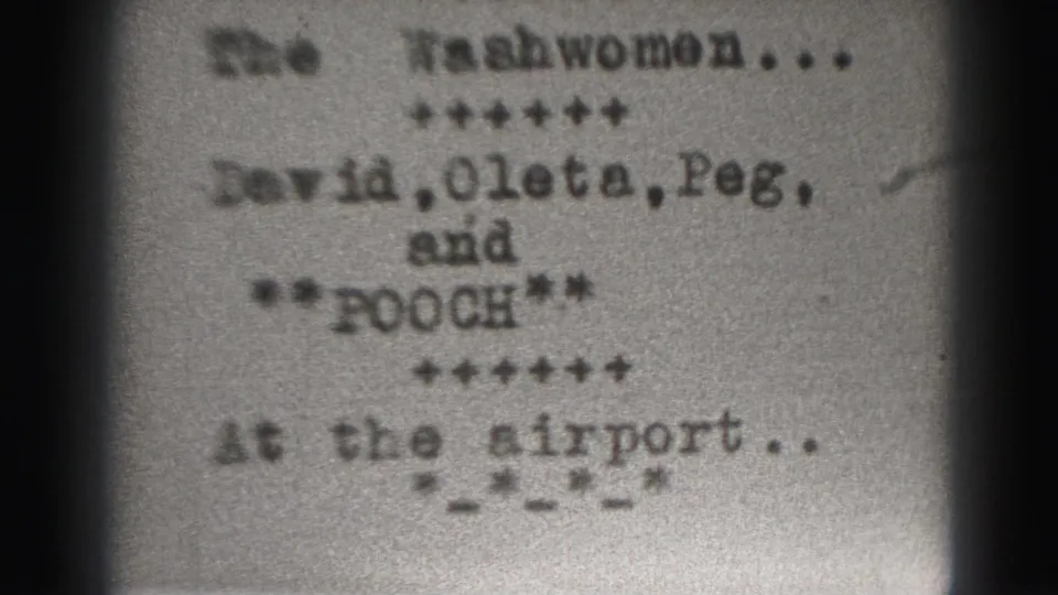 Blurred 8mm title-card frame tied to the Harrisburg clip, showing The Washwomen text and an at-the-airport line.