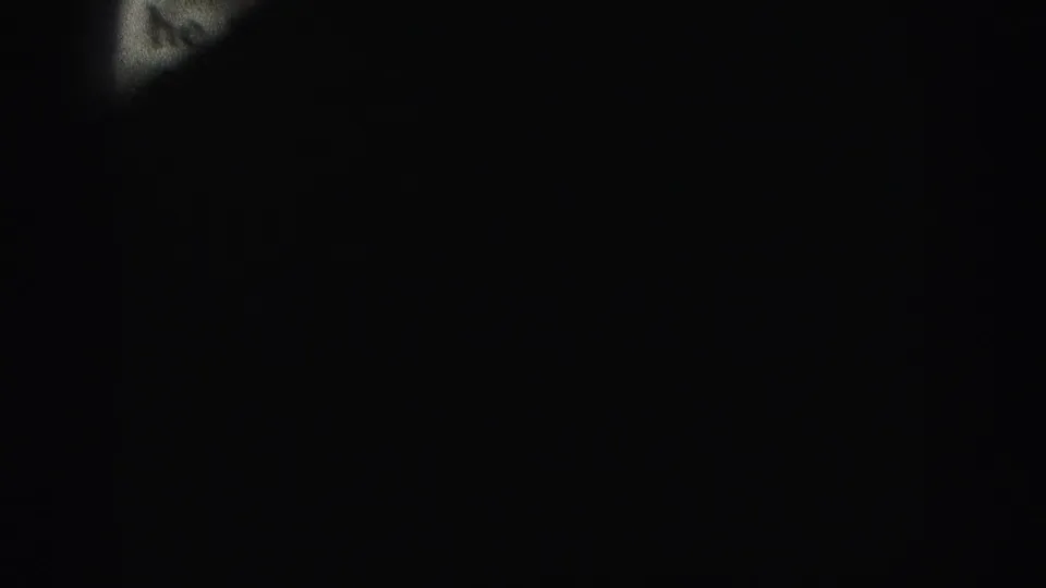Dark transition frame from the 8mm reel, with only a small pale portion of the previous paper object visible at the top edge.