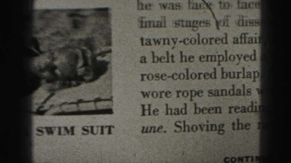 Newspaper clipping showing two columns of text and a small printed photograph captioned SWIM SUIT, seen in soft 8mm focus.