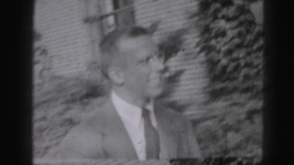 1946 Harrisburg frame of a suited adult man in profile during an outdoor greeting, with another figure partly visible near the edge.