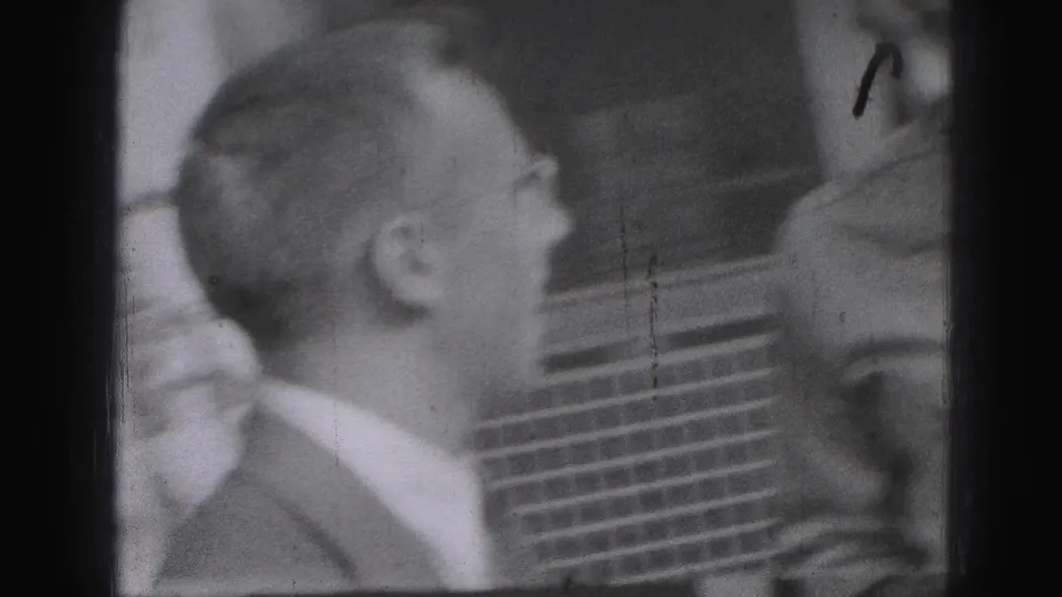 1946 Harrisburg frame showing a suited adult man in side view facing another person near a brick wall or dark exterior detail.