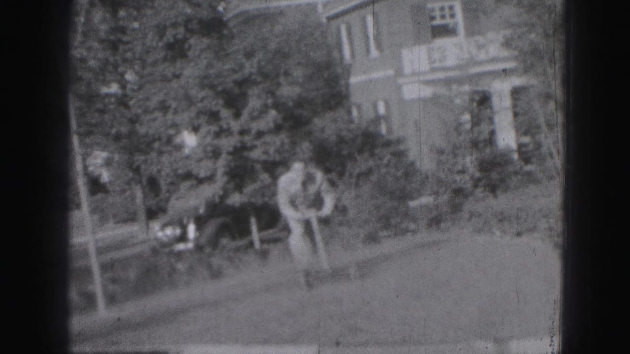 Man in a yard bends near a small wheeled toy with a house and parked car behind him.