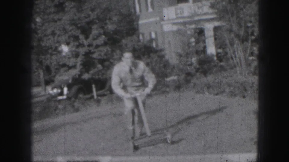 A man in a light shirt and tie appears to handle a small toy vehicle in a Harrisburg residential yard in 1946 home-movie footage.