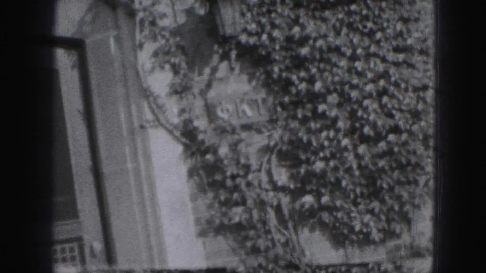 A tilted 1946 Harrisburg home-movie frame shows ivy on a house exterior with windows and a partial yard view.