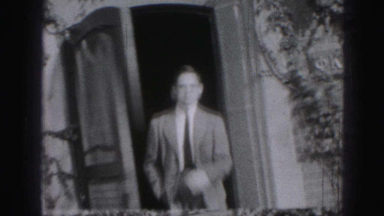 Adult man in a suit stands in an open doorway beside the house exterior.