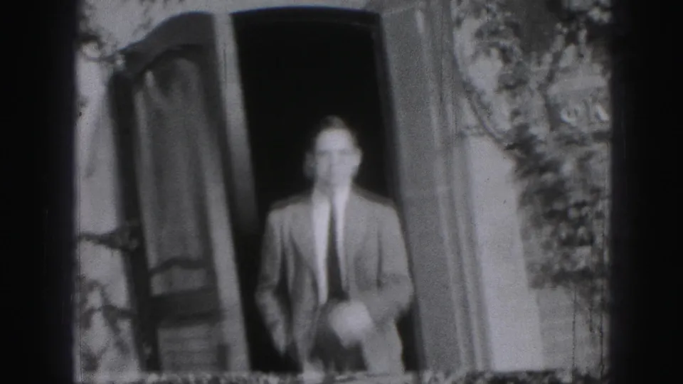 Adult man in a suit and tie stands in a Harrisburg house doorway in black-and-white 1946 home-movie footage.