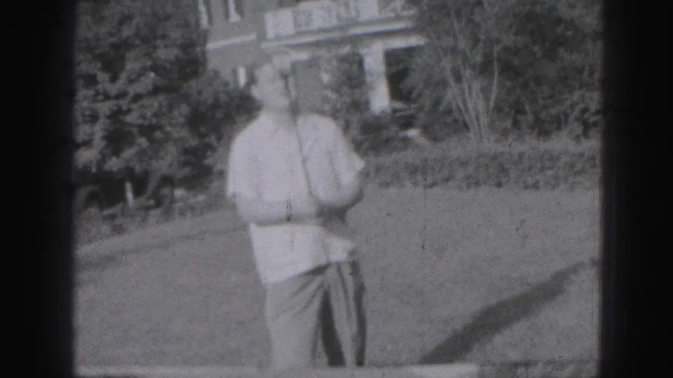 Adult man appears to practice golf on a Harrisburg lawn, with shrubs and a house in the background.