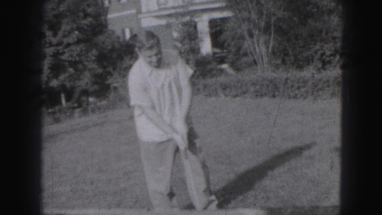 In 1946 Harrisburg home-movie footage, a man in a light shirt stands on a grassy yard with a golf club, trees and a house behind him.