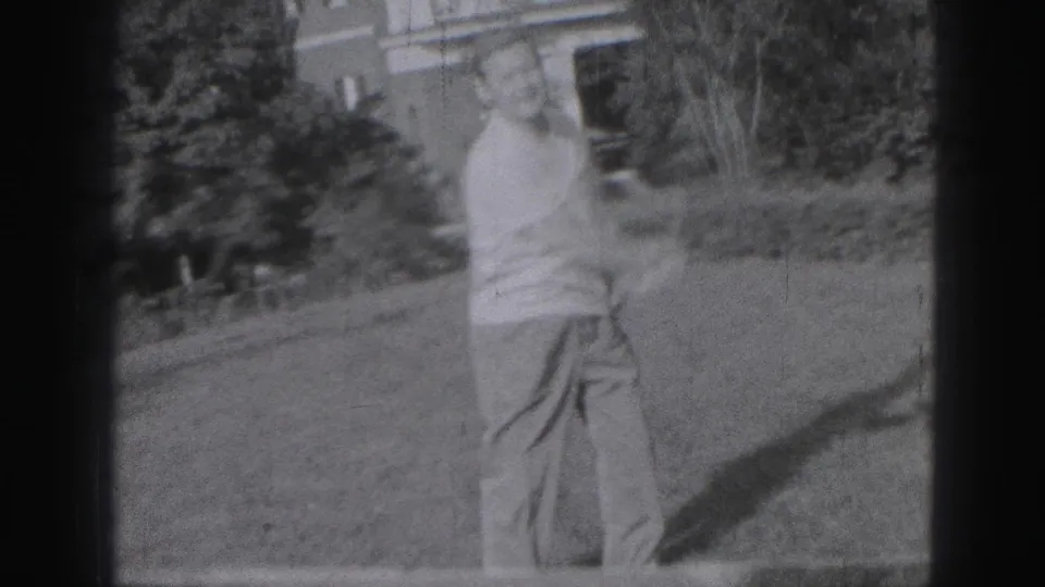 The man follows through after a golf swing in the 1946 Harrisburg yard scene, framed by lawn, shrubs, and 8mm film borders.