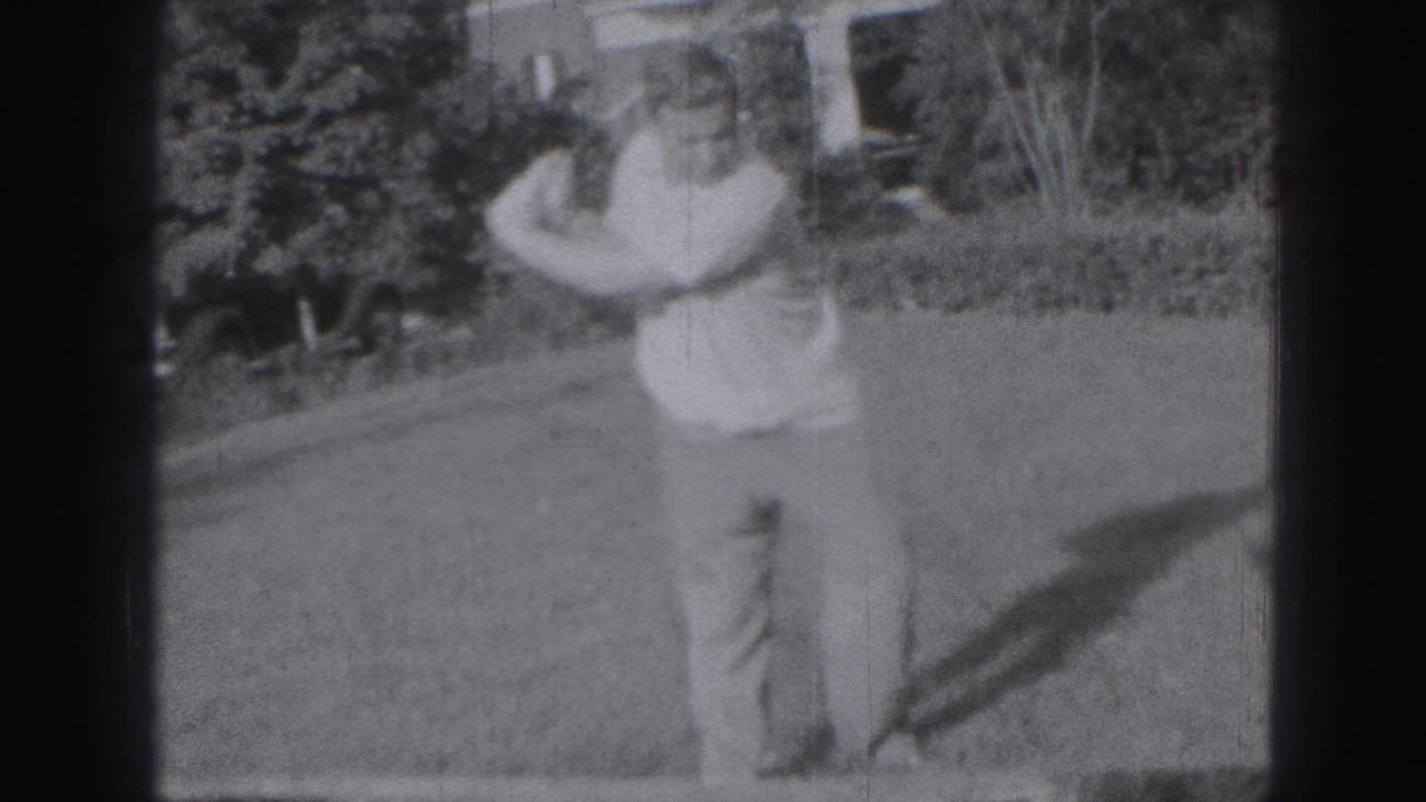 Man on a lawn holding a golf club near trees and a house.