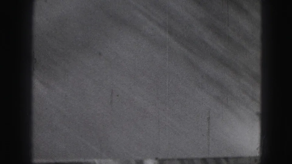A sparse frame from the 8mm clip shows lawn or pavement texture with dark vertical film borders and little subject detail.
