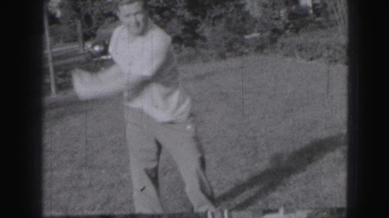 Adult man begins a golf swing on grass in black-and-white home-movie footage.