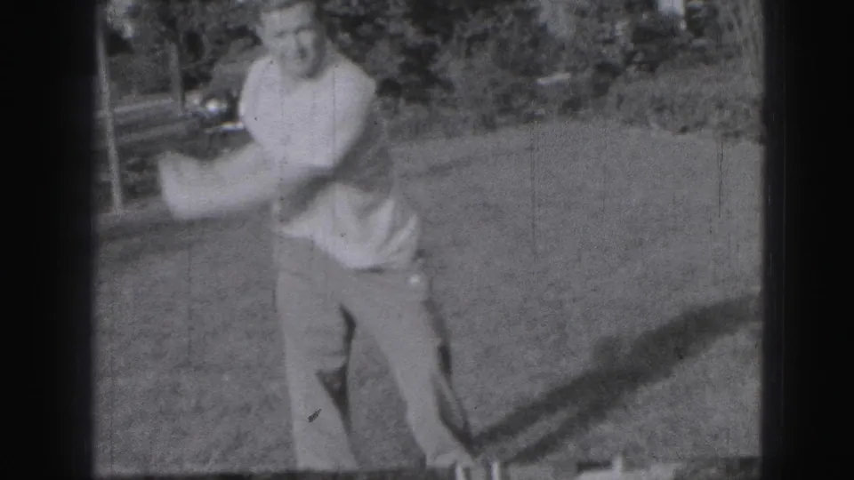 Adult man in a short-sleeve shirt and trousers starts a golf swing on a grassy Harrisburg setting in 1946 home-movie footage.