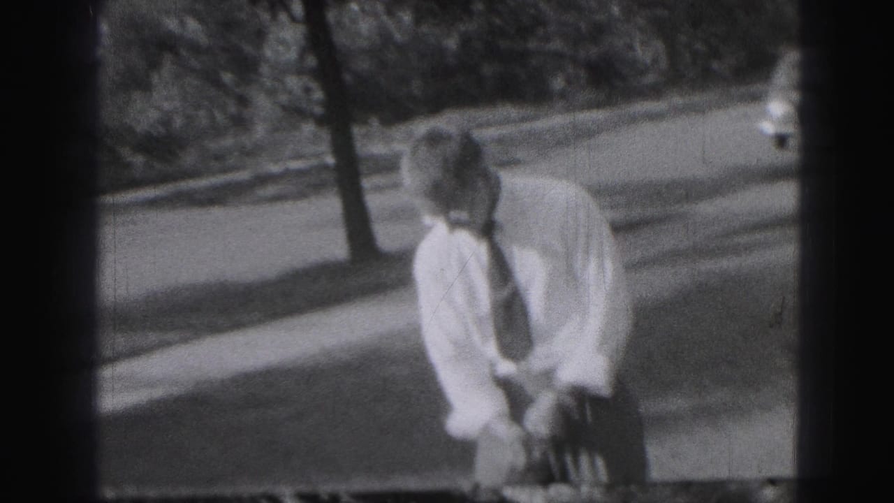 Man in a white shirt and tie bends over a golf club on grass near a street.