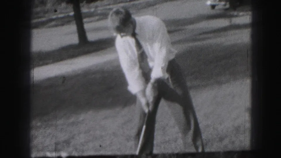 An adult man in shirt and tie holds a golf club on a grassy area near a tree-lined street in Harrisburg, Pennsylvania, in 1946.