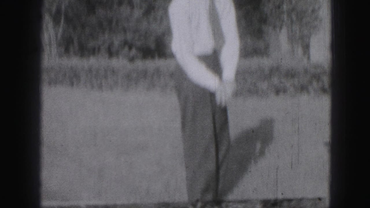 Man standing on a lawn with a golf club lowered in front of him.