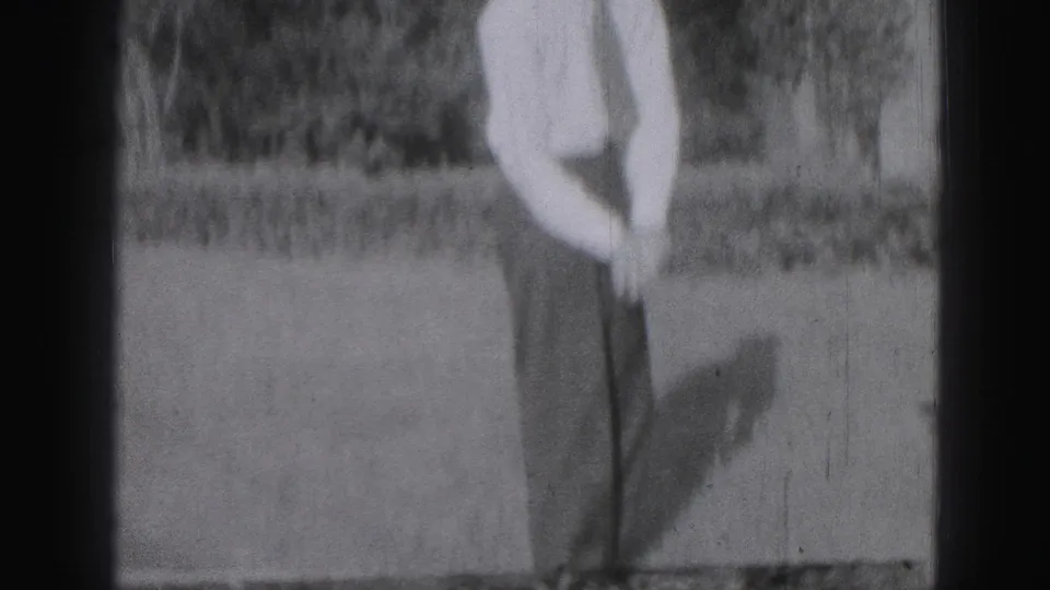 In Harrisburg, Pennsylvania in 1946, a man in a light shirt and dark trousers stands on a lawn holding a golf club.