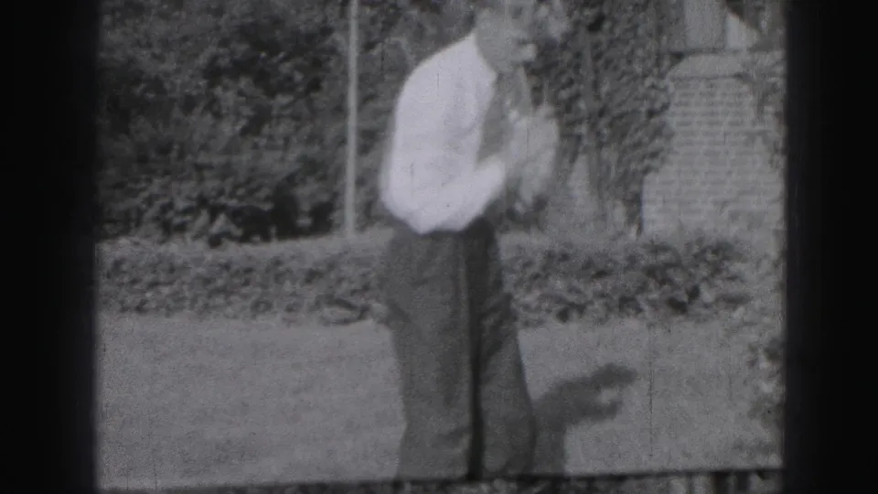 A man in shirt and trousers follows through a golf practice motion on a residential lawn in 1946 Harrisburg footage.
