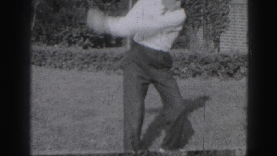 The man finishes a golf swing on the lawn, with motion blur from the club and soft 8mm black-and-white texture.