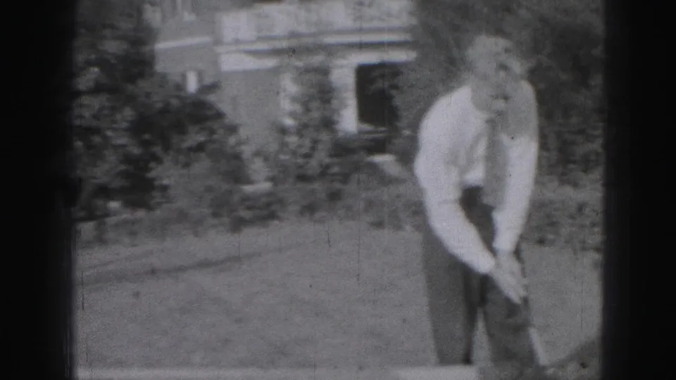 In 1946 Harrisburg home-movie footage, a man in a white shirt and tie prepares a golf swing on a grassy residential lawn.