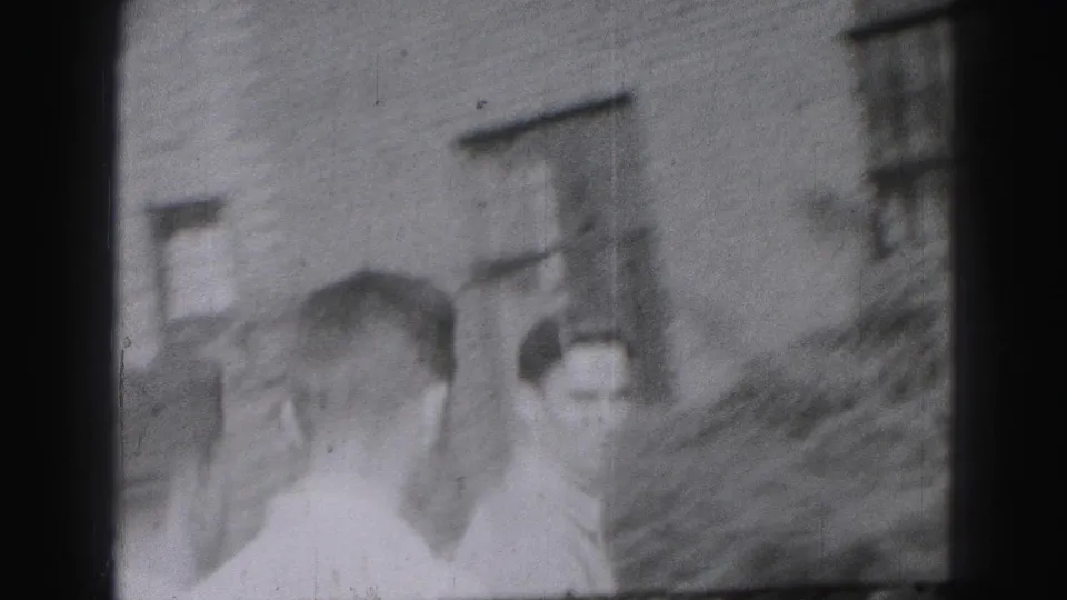 Several young men appear together outside a masonry building, with one figure seen from behind in the foreground.