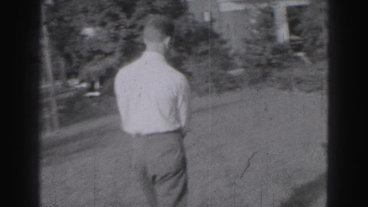 Man in a light shirt and dark trousers walks across a Harrisburg garden lawn in a 1946 8mm home movie.