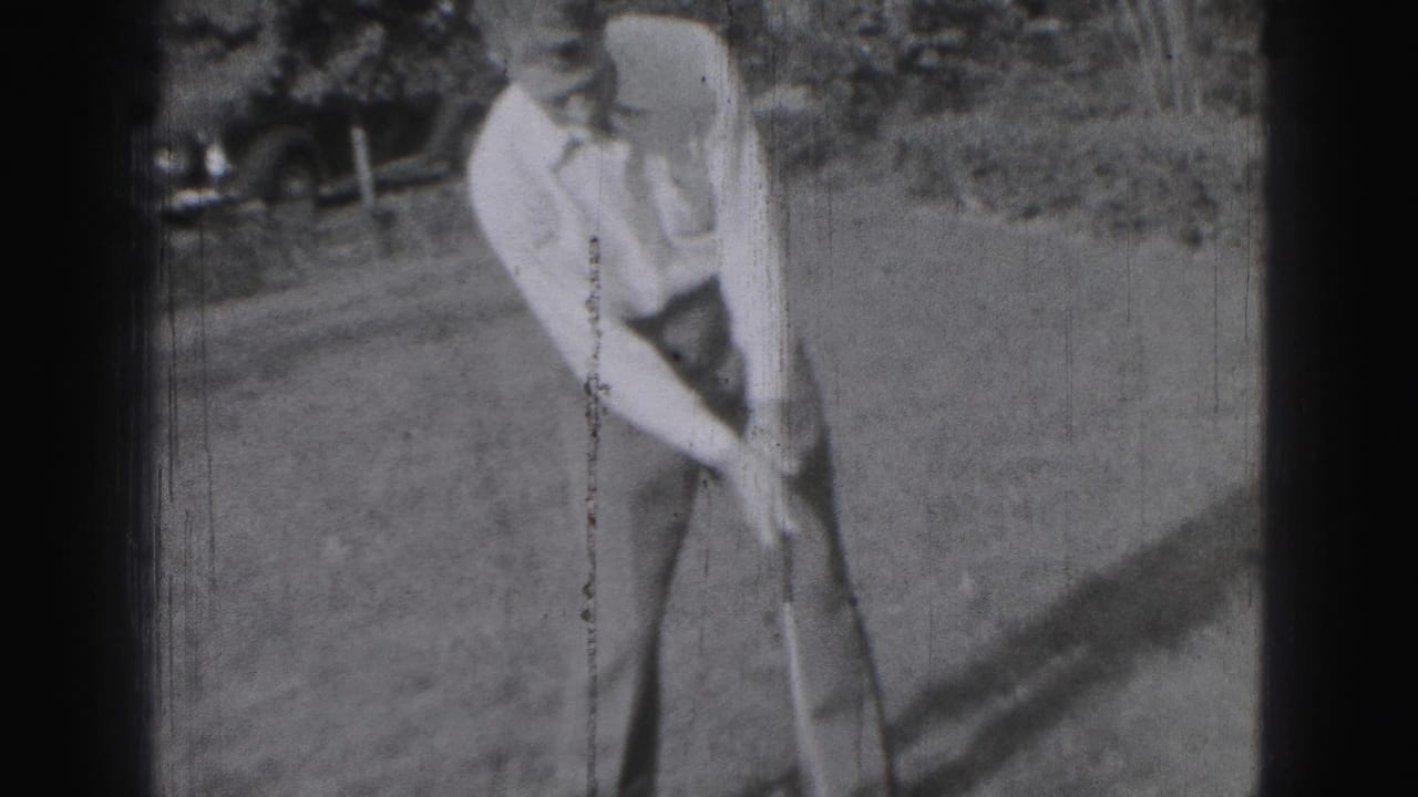 Black-and-white 8mm frame from Harrisburg in 1946 showing a golfer addressing the ball, with an older car visible behind the lawn.