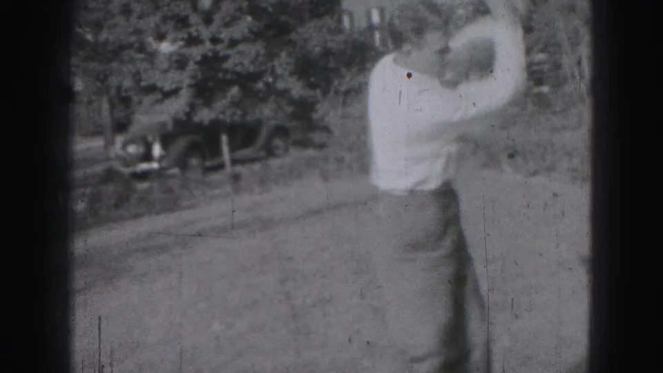 Adult man plays golf on a grassy course near Harrisburg in 1946, with a vintage car partly visible behind trees.