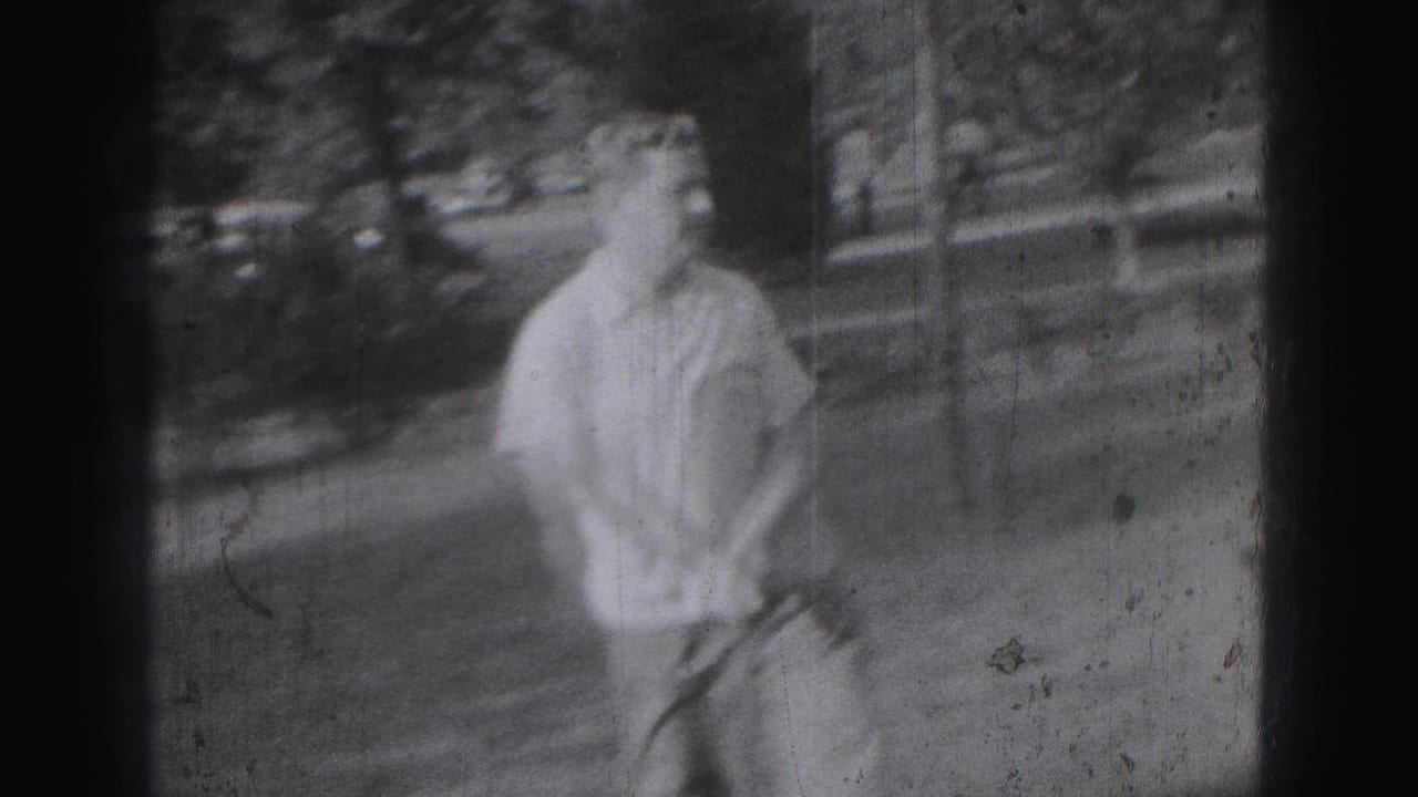 Adult man on a 1946 Harrisburg grass course holds a golf club after a swing, framed in soft black-and-white 8mm footage.