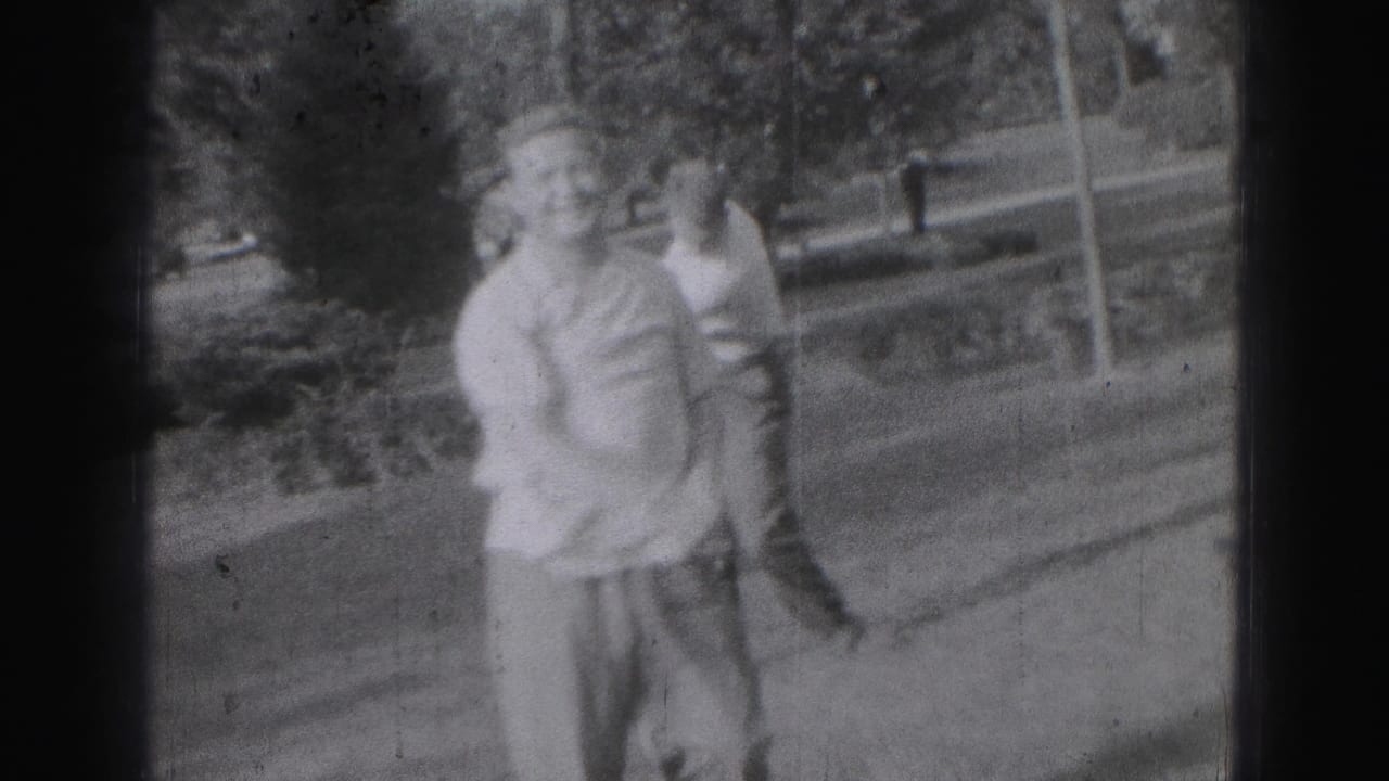 Two young men stand together outdoors near a lawn and trees.
