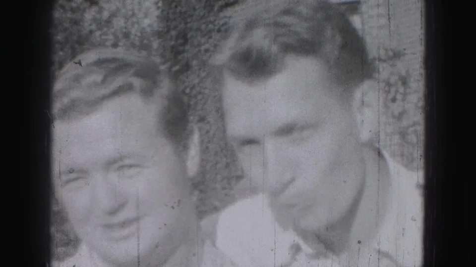 Two adult men in light shirts smile or lean toward the camera in 1946 Harrisburg home-movie footage.