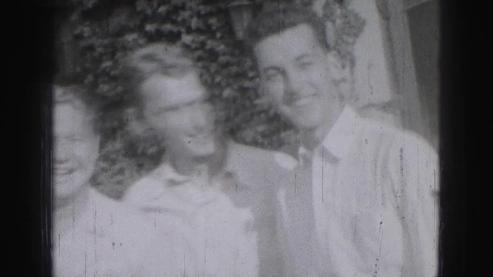 Adult men in light shirts gather closely outdoors in a 1946 Harrisburg home-movie frame, with two faces clearly visible and one partly cropped.