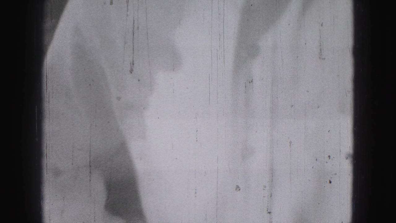 Blurred partial figure near a pale vertical surface in a scratched film frame.