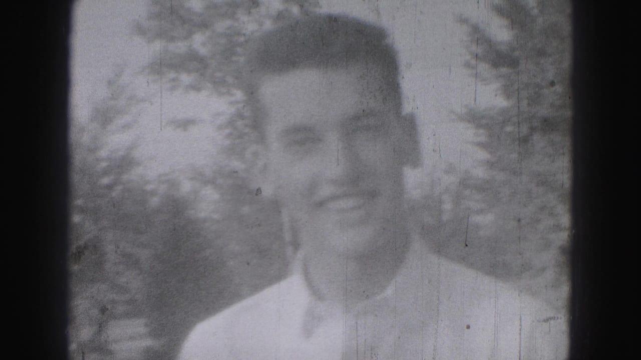 Adult man in a light shirt seen in soft focus with trees behind him.